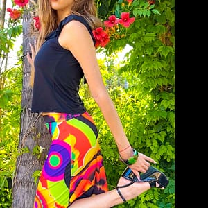 Fotografía de una mujer con un top con volantes de color negro y una falda muy colorida de colores vibrantes con círculos y flores.