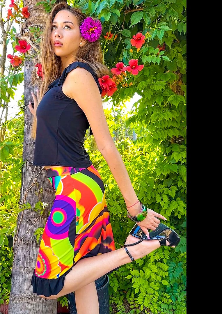 Fotografía de una mujer con un top con volantes de color negro y una falda muy colorida de colores vibrantes con círculos y flores.