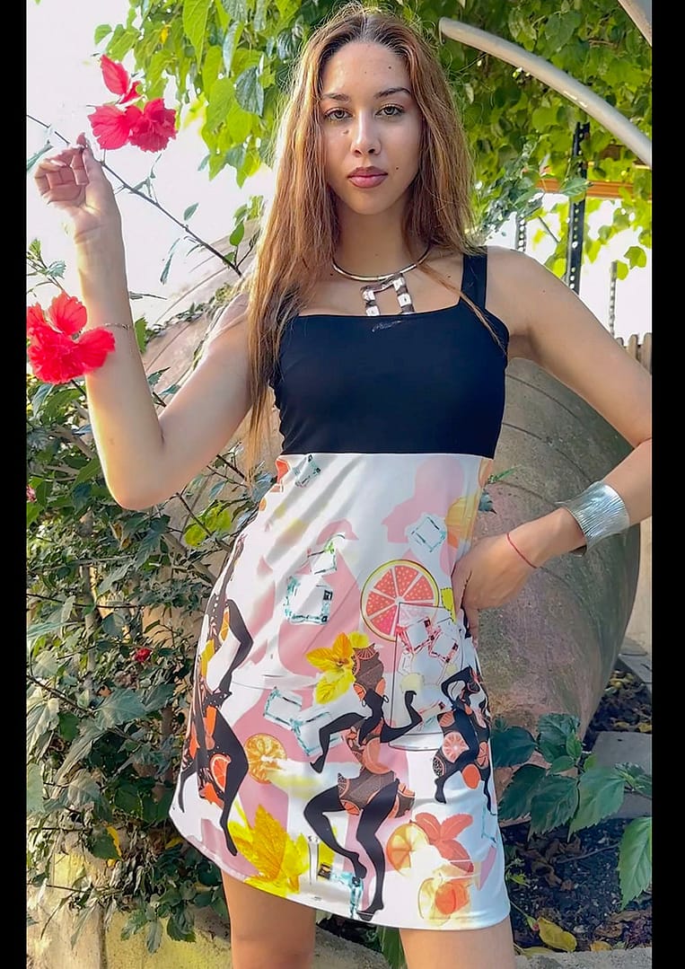 Fotografía de una mujer con un vestido donde la parte de arriba es negra y en la parte de abajo, tiene motivos que recuerdan a Cuba, con mojitos con hielo y mujeres vestidas todas diferente.